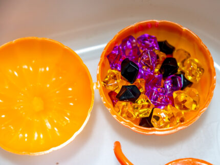 Halloween Bear Sensory Bin with colorful Halloween rice, costumed bears, ghosts, spider, pom-poms, gems, pumpkin container and wooden scoop