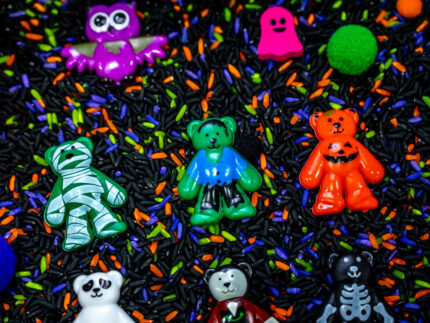 Halloween Bear Sensory Bin with colorful Halloween rice, costumed bears, ghosts, spider, pom-poms, gems, pumpkin container and wooden scoop