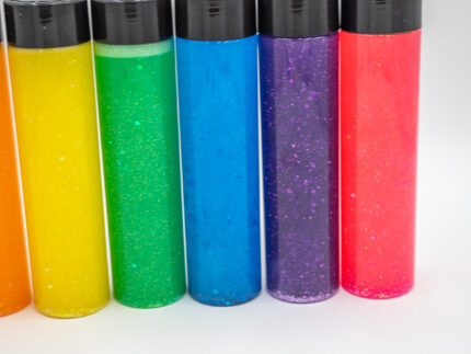 Six glitter calming bottles in pink, orange, yellow, green, blue, and purple with sparkly glitter