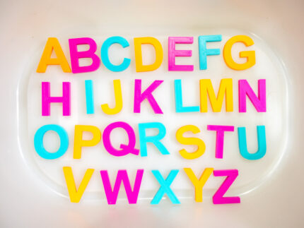 Chicka Chicka Alphabet Sensory Bin with colorful sensory filler, alphabet letters, coconut container, palm trees, pom-pom coconuts and wooden scoop