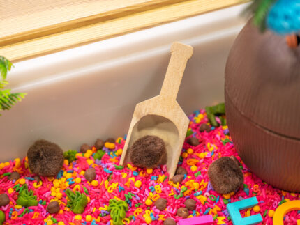Chicka Chicka Alphabet Sensory Bin with colorful sensory filler, alphabet letters, coconut container, palm trees, pom-pom coconuts and wooden scoop