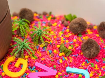 Chicka Chicka Alphabet Sensory Bin with colorful sensory filler, alphabet letters, coconut container, palm trees, pom-pom coconuts and wooden scoop