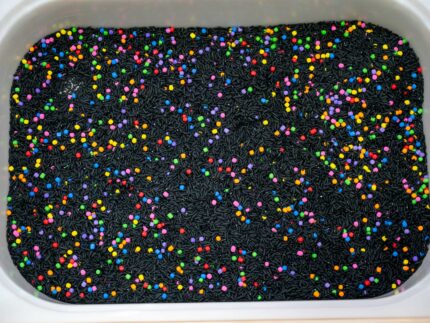 Trick-or-Treat Sensory Bin with black rice, rainbow couscous, pumpkin containers, pretend candy, ghosts, pom-poms, and wooden scoop