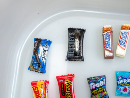 Trick-or-Treat Sensory Bin with black rice, rainbow couscous, pumpkin containers, pretend candy, ghosts, pom-poms, and wooden scoop