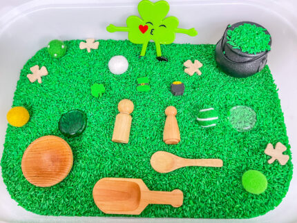 St. Patrick’s Day sensory bin with green rice, shamrocks, pot of gold, wooden peg people and wooden scoop