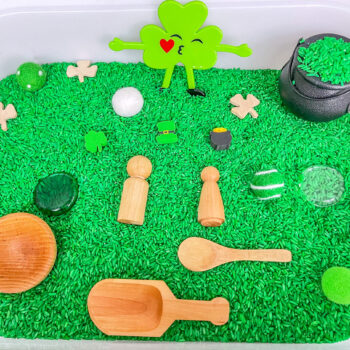 St. Patrick’s Day sensory bin with green rice, shamrocks, pot of gold, wooden peg people and wooden scoop